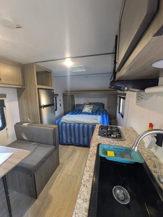 RV rental: compact interior features kitchen, dining booth, refrigerator, and a cozy bed with blue bedding.. Sunset Park & Rv Inc. 19rb 2025