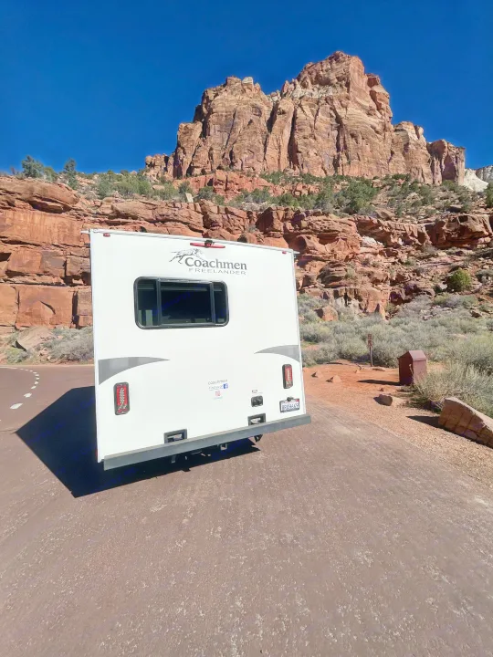 White Coachmen Freelander RV rental parked on a road, with majestic red rock mountains and a clear blue sky behind it.. Forest River Coachmen Freelander 2019