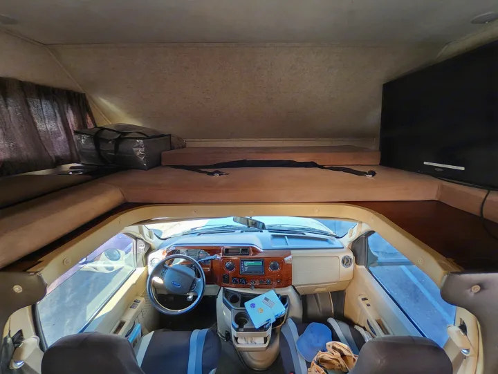 RV rental interior: driver's cab with steering wheel, dashboard, and an overhead bunk with mattress, TV. Ready for road trip travel.. Forest River Other 2018