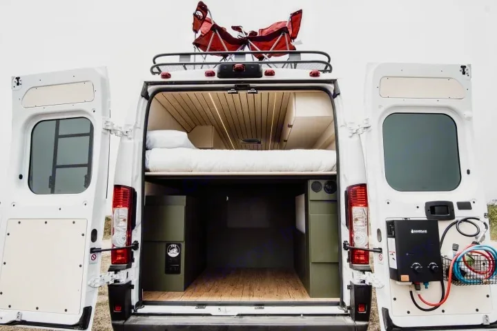 This RV rental reveals a camper van's open rear, showcasing a cozy bed, storage, and outdoor shower setup, perfect for adventure.. Ram ProMaster 2022