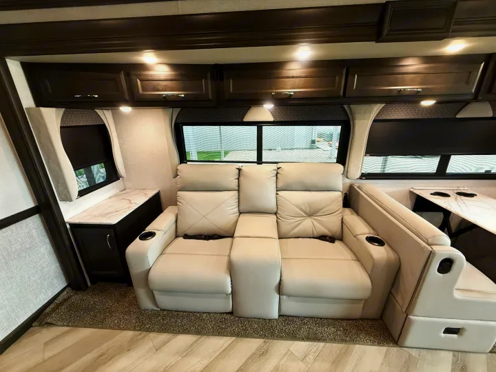 Inside a modern rv rental: Cream recliners, a dinette, dark overhead cabinets, and windows create a comfy space.. Bounder Bounder Motorhome 2024