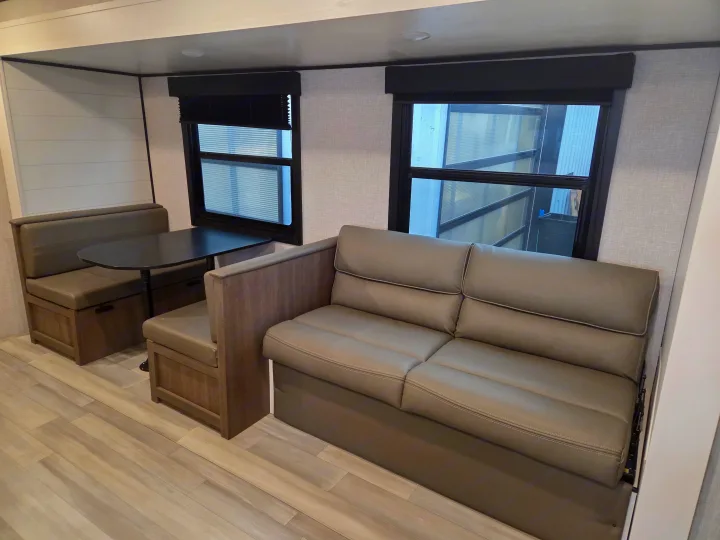 This modern RV rental interior features a practical dinette with bench seating & table, plus a comfortable sofa. Ideal for travel comfort.. Open Range Conventional 26BHS Travel Trailer 2025