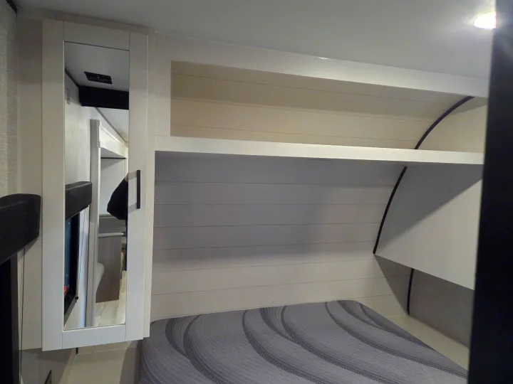 Modern RV rental bedroom featuring a mirrored cabinet, storage shelf, and striped grey bed for a comfortable stay.. Open Range Conventional 26BHS Travel Trailer 2025