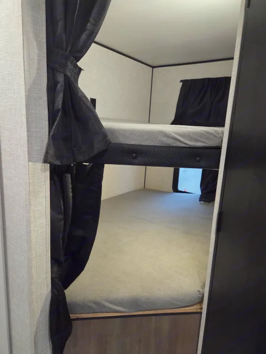 RV rental: Bunk beds with tied-back dark privacy curtains, light grey mattresses, and textured walls create a cozy sleeping space.. Open Range Conventional 26BHS Travel Trailer 2025