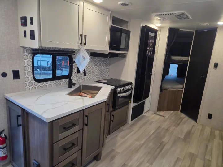 Bright rv rental kitchen with white countertops, black faucet, oven, microwave, fridge, and bunk beds, perfect for family travel.. Open Range Conventional 26BHS Travel Trailer 2025