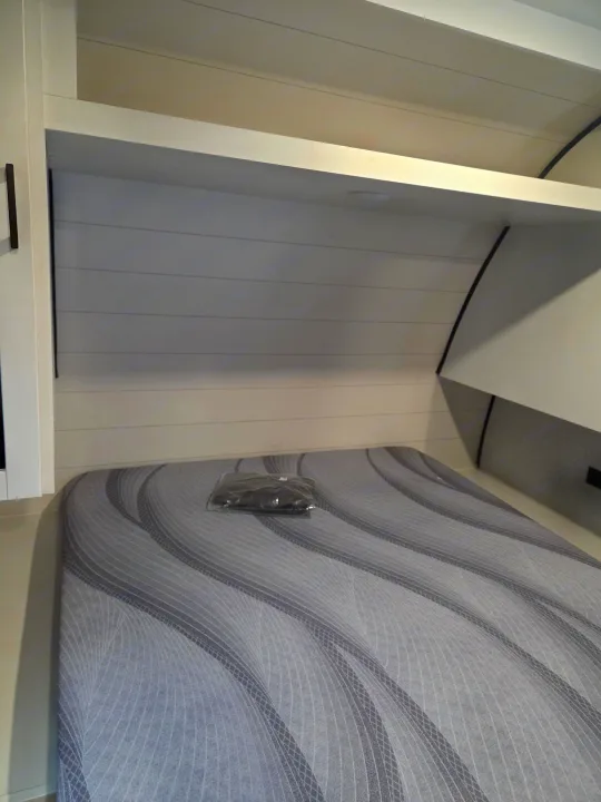A clean RV rental bedroom features a gray patterned bed, white shiplap headboard, and an overhead shelf for storage.. Open Range Conventional 26BHS Travel Trailer 2025