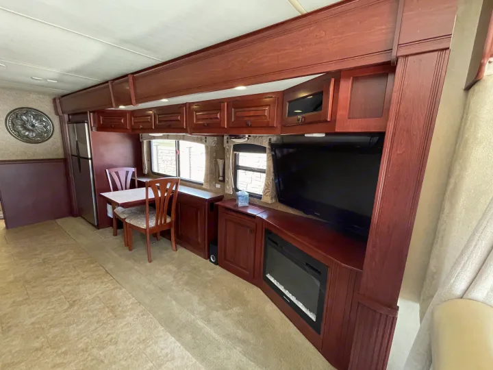 RV rental interior: inviting living space with rich wood cabinets, dining area, flat-screen TV, and electric fireplace.. Berkshire Berkshire Motorhome 2013