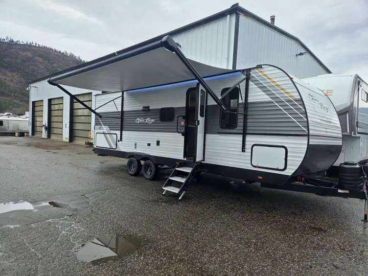 RV rental: Open Range travel trailer with extended awning & LED lights, parked on a wet lot. Ready for adventure!. Open Range Conventional 26BHS Travel Trailer 2025