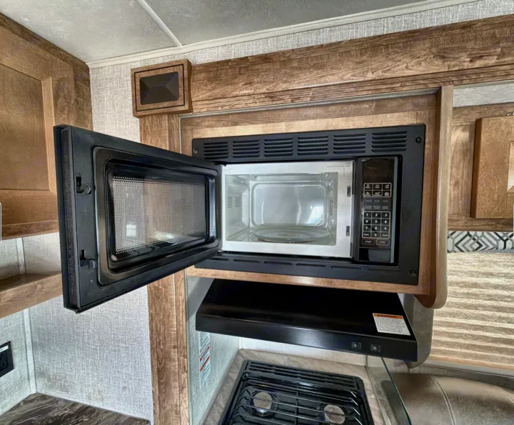 Compact RV rental kitchen with an open microwave, range hood, and two-burner stove for convenient cooking on the go.. Coachman Leprachaun 2020