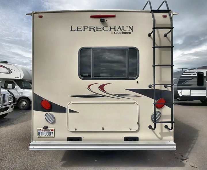 Rear view of a tan "Leprechaun by Coachmen" RV, ideal for an rv rental. It features a ladder, window, and tail lights.. Coachman Leprachaun 2020