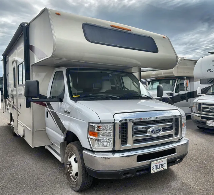 White Class C motorhome, a Ford RV rental, parked on asphalt under a cloudy sky, ready for your next travel adventure.. Coachman Leprachaun 2020
