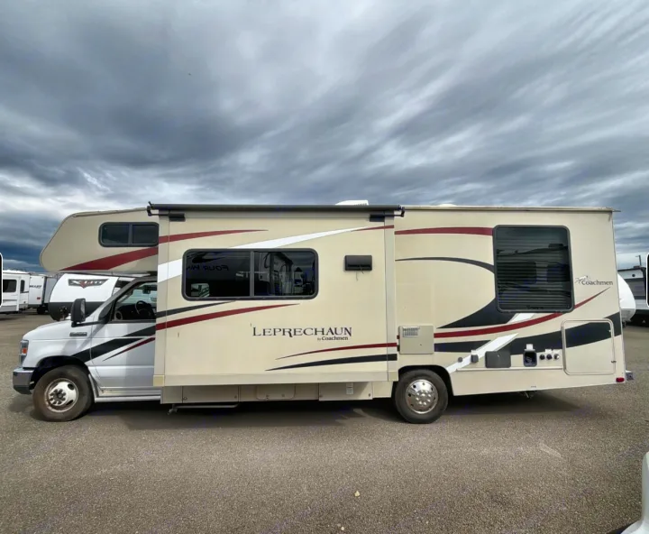 A cream Coachmen Leprechaun Class C motorhome, an excellent RV rental option, parked with its slide-out extended.. Coachman Leprachaun 2020
