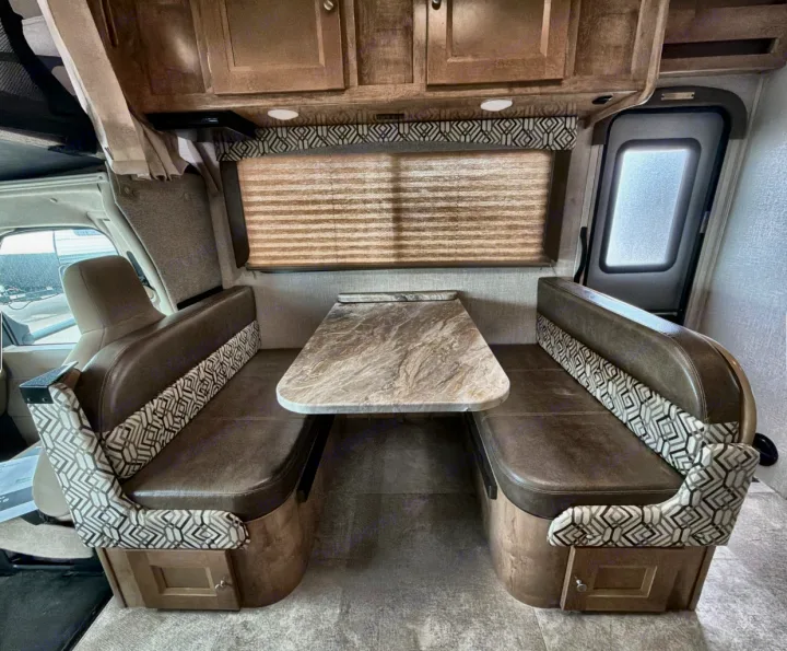 RV rental dinette with cozy booth seating, a table, and overhead cabinets, ideal for meals or relaxing on your journey.. Coachman Leprachaun 2020