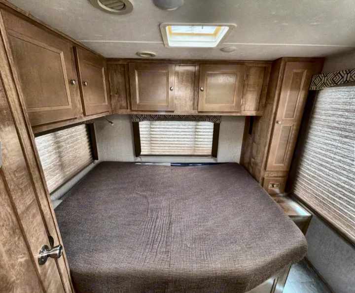 RV rental: Interior shot of a bedroom with a large brown bed, overhead wood cabinets, and window blinds.. Coachman Leprachaun 2020