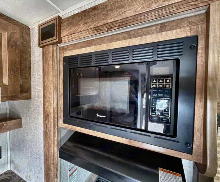 Black built-in microwave oven with a control panel and glass door in an rv rental kitchen, surrounded by warm wooden cabinetry.. Coachman Leprachaun 2020