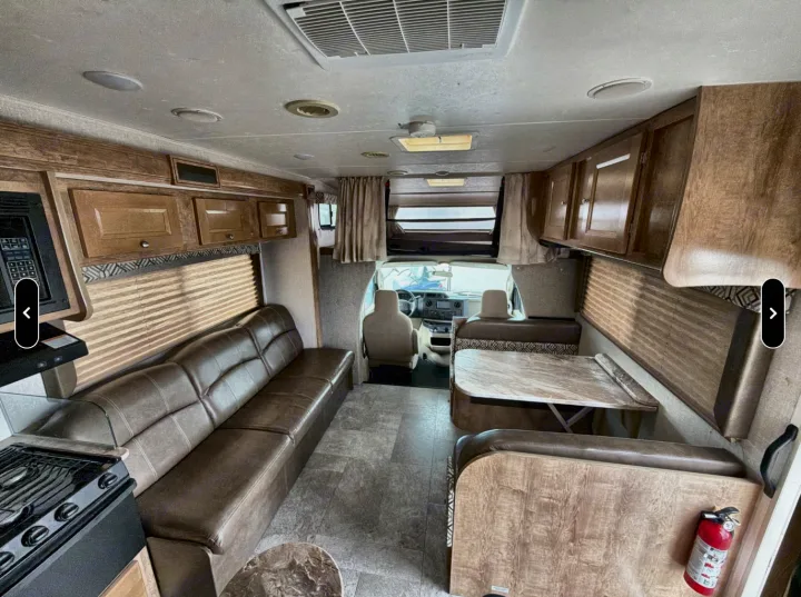 Spacious RV rental interior featuring a long sofa, dinette with table, and compact kitchen area.. Coachman Leprachaun 2020