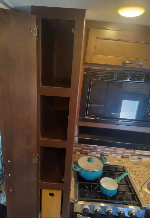 An RV rental kitchen featuring open brown cabinets, a microwave, and a stovetop with two blue pots for cooking.. Thor Motor Coach Four Winds 2017