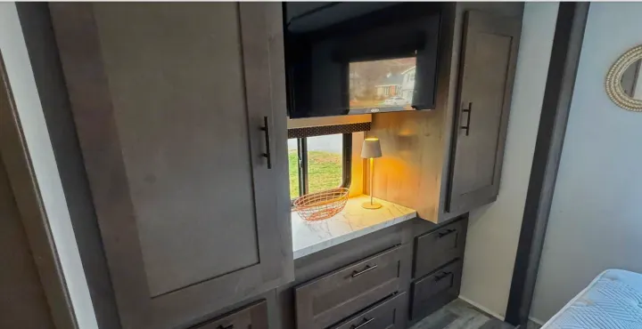 Modern RV rental bedroom featuring a built-in TV, counter space with a lamp, window view, and ample storage cabinets.. FR3 FR3 Motorhome 2023