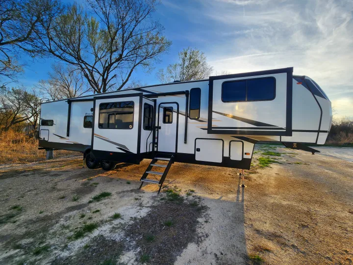 Modern fifth-wheel rv rental with extended slides and deployed steps, parked on a dirt lot under a blue sky.. phoenix 334FL 2026