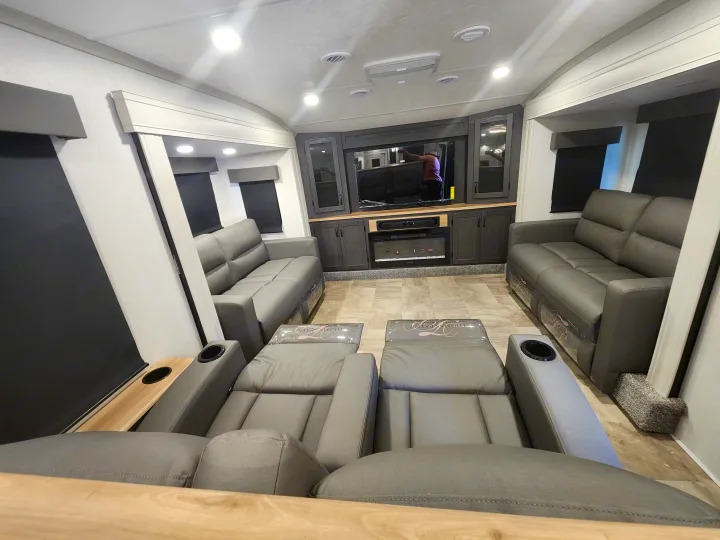 Luxurious RV rental living area with comfortable recliners (cup holders visible), plush sofas, and a modern entertainment center with a fireplace.. phoenix 334FL 2026