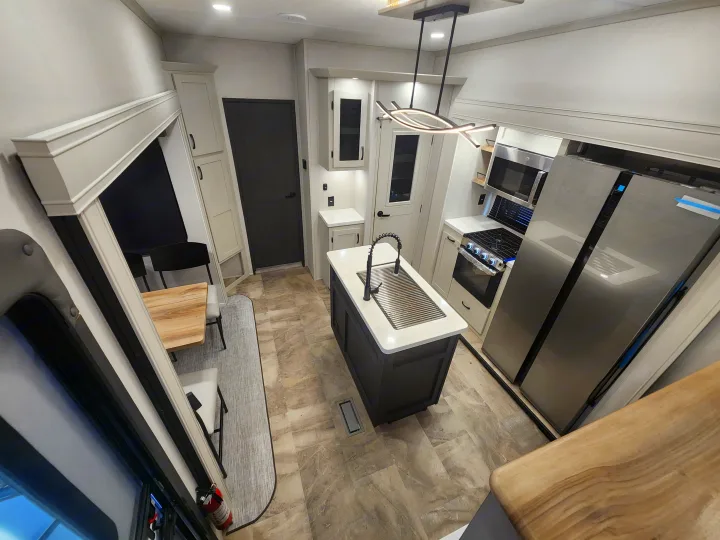 Modern RV rental interior showing a spacious kitchen with island sink, stainless steel appliances, and adjacent dining area.. phoenix 334FL 2026