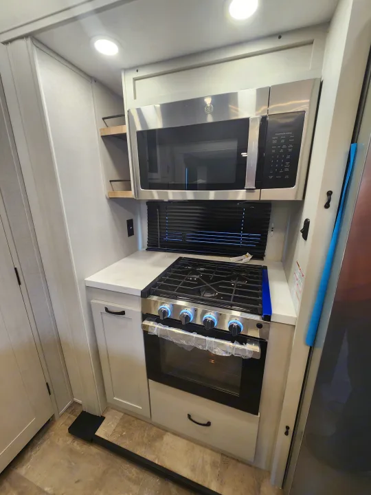 Modern RV rental kitchenette featuring a stainless steel microwave, 4-burner gas stove with blue-lit knobs, and oven.. phoenix 334FL 2026