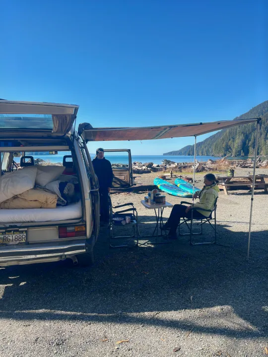 An rv rental adventure: A pop-top camper van by the ocean with an awning, paddleboards, and people relaxing.. Volkswagen Westfalia 1986