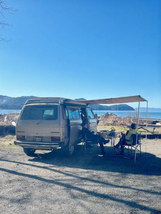 Experience van life! This RV rental, a tan VW Westfalia, offers a scenic waterfront camping spot for two under an awning.. Volkswagen Westfalia 1986