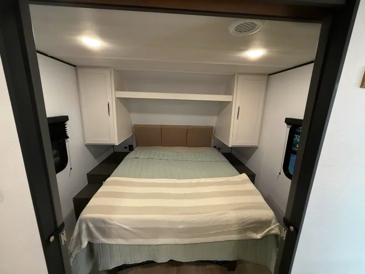 Cozy and compact RV rental bedroom featuring a comfortable bed, overhead storage, and side windows.. Keystone Bullet 2026