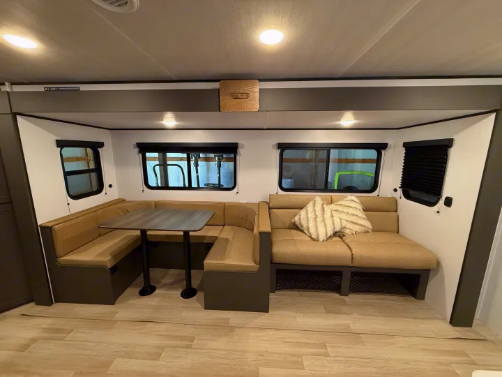 Cozy RV rental interior: U-shaped dinette, sofa with a fluffy pillow, large windows. Light wood-look floor completes the comfortable living space.. Keystone Bullet 2026