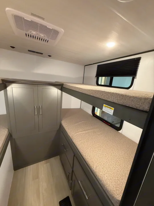 Comfortable RV rental interior: two bunk beds with light mattresses, gray storage cabinets, and a ceiling AC unit.. Keystone Bullet 2026