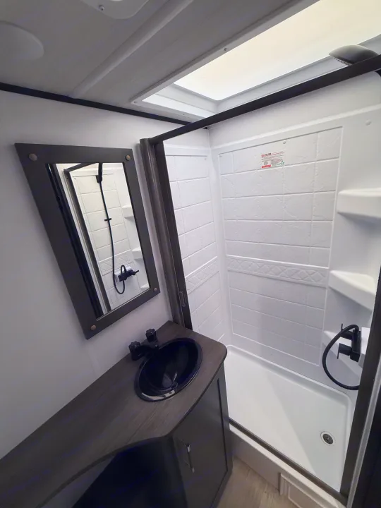 Compact RV rental bathroom with a dark vanity, black sink, mirror, and a stand-up shower stall featuring a skylight.. Keystone Bullet 2026