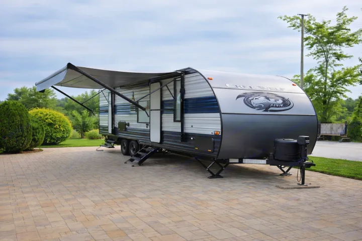 Cherokee Wolf travel trailer, ideal for your next RV rental. Grey & blue RV with extended awning on pavers.. Forest River Cherokee Grey Wolf 2020