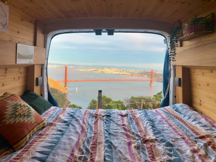 An rv rental's cozy bed offers panoramic views of the Golden Gate Bridge and San Francisco Bay from inside a wooden camper van.. Ford Transit 2019