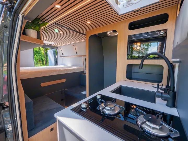 Explore this modern RV rental interior! Features a compact kitchen, comfy bed, & seating under a stylish wooden ceiling.. Fiat Ducato 2025