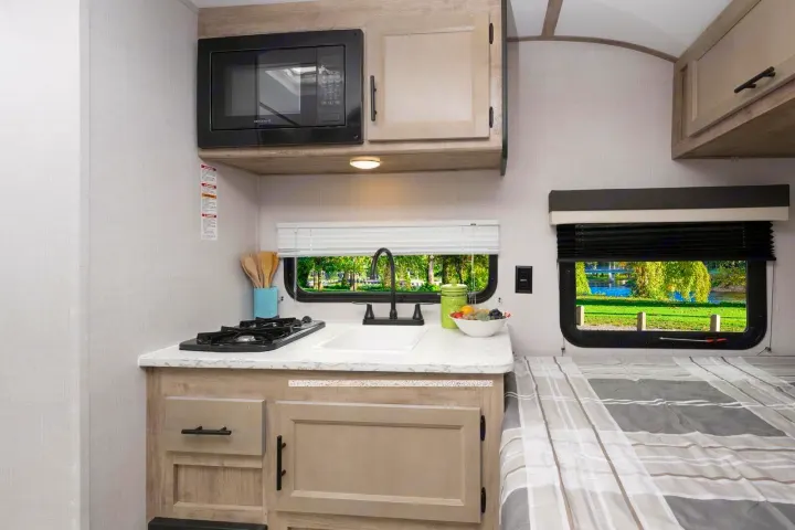 Compact RV rental interior featuring a functional kitchen with microwave, sink, and stovetop, alongside a cozy sleeping area.. Gulf Stream Ameri-Lite Super Lite 2023