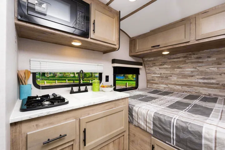 Compact rv rental interior featuring a kitchenette with a microwave, sink, and stove, adjacent to a cozy bed.. Gulf Stream Ameri-Lite Super Lite 2023