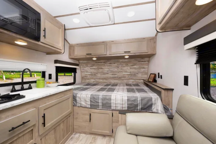 Cozy RV rental interior shows kitchenette, built-in bed, and sofa. Light wood finishes & clever storage maximize compact space.. Gulf Stream Ameri-Lite Super Lite 2023