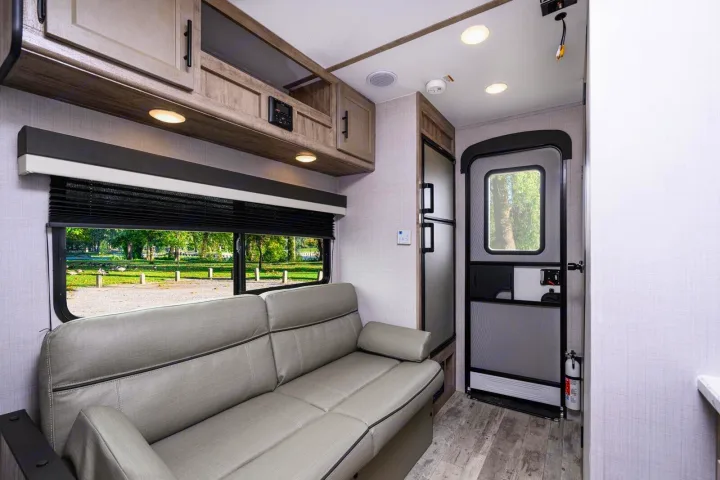 RV rental: Modern RV living area with a comfortable gray sofa, large window showcasing a park view, and compact fridge.. Gulf Stream Ameri-Lite Super Lite 2023