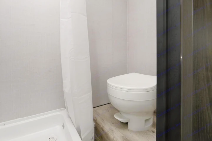 Compact RV rental bathroom featuring a white toilet, shower pan, and curtain against textured grey walls and wood-look flooring.. Gulf Stream Ameri-Lite Super Lite 2023