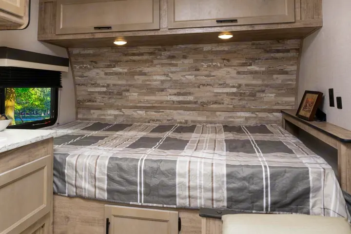 Cozy RV rental bedroom with a comfortable bed, overhead storage, and a scenic window view of nature.. Gulf Stream Ameri-Lite Super Lite 2023