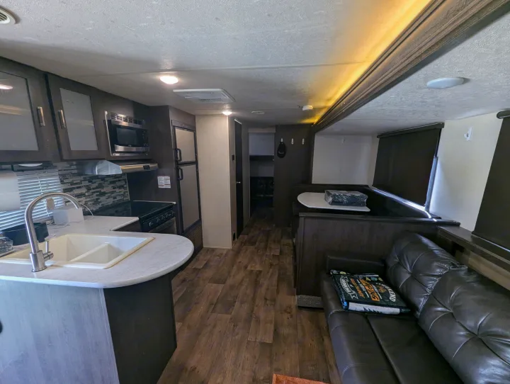 View of an rv rental's interior, showcasing a full kitchen, wood flooring, and a living area with a dark sofa and dinette.. Forest River Salem Cruise Lite 2018