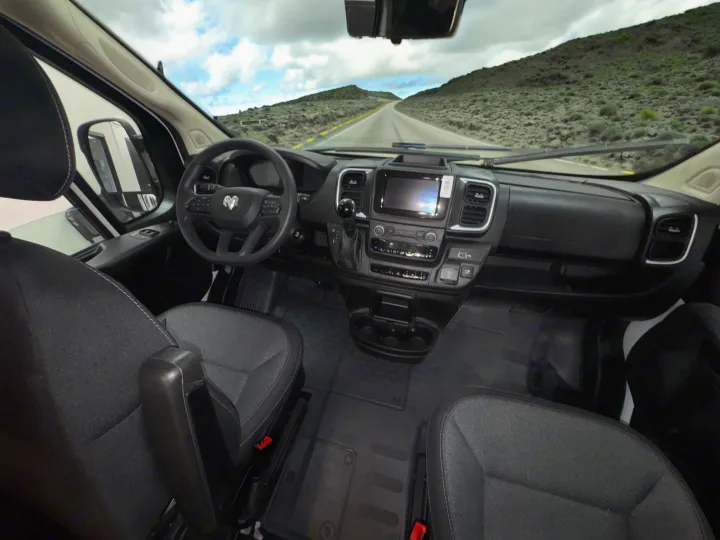 RV rental. Driver's seat view of a camper van's interior: dash, steering wheel, seats, and open road ahead.. Winnebago Solis 2025