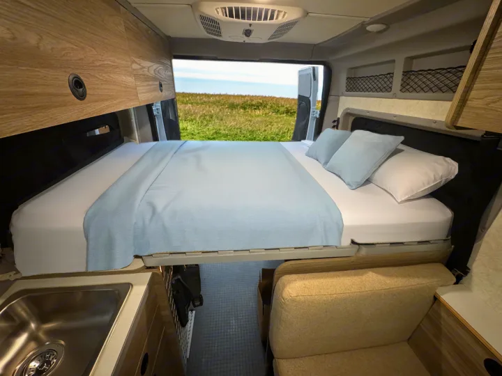 Enjoy comfort in this RV rental: a cozy bed, handy sink, and stunning nature views through open back doors.. Winnebago Solis 2025