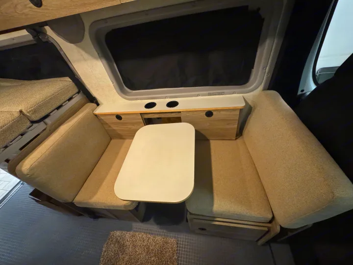 RV rental interior: A compact dining area with cushioned benches, a removable table, built-in storage, and window, ideal for travel.. Winnebago Solis 2025