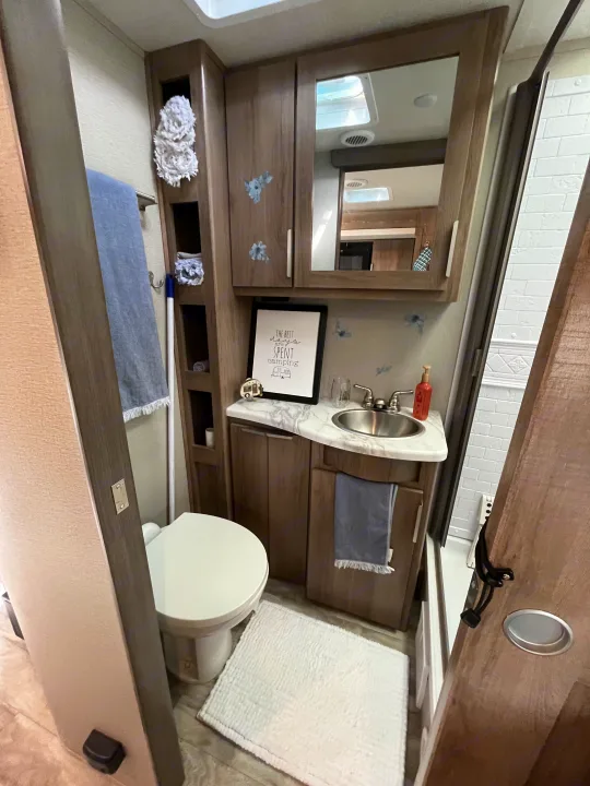 Compact RV rental bathroom with toilet, sink, mirror cabinet, and fun camping decor.. Grand Design Imagine XLS 2021