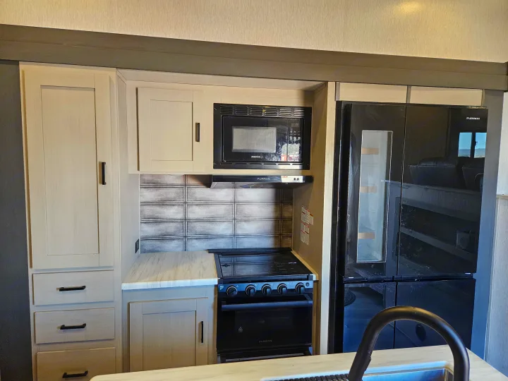 Modern RV rental kitchen featuring a microwave, stovetop, large refrigerator, and light-colored cabinets.. Forest River Hemisphere 2021