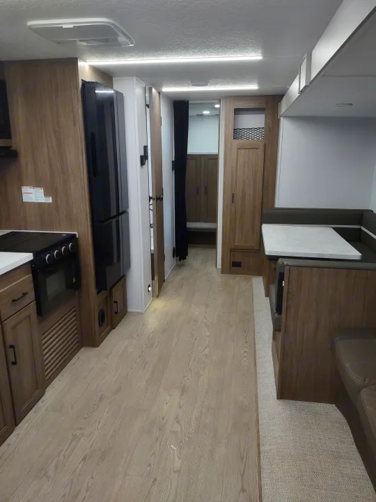 View inside a modern rv rental with kitchen, dining area, light wood flooring, and bright overhead lights.. Coachmen 29 SE 2025