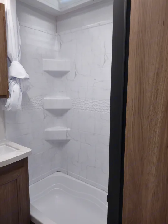 RV rental bathroom: modern white shower with marble-look walls & built-in shelves, plus a compact sink. Clean & functional.. Coachmen 29 SE 2025