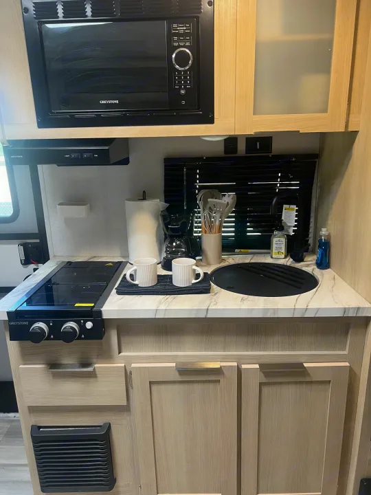 Compact rv rental kitchen: Greystone microwave, stovetop, sink, coffee maker, mugs, and cooking essentials.. Forest River Salem FSX 2023